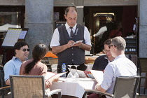 Spain, Madrid, Waiter taking orders from diners at a restaurant in the Plaza Mayor.