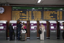 Spain, Madrid, Passengers using the self-service ticket machines in front of the departures board inside the terminus of the Atocha Railway Station.