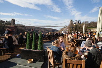 England, Bristol, Drinkers on the terrace of the White Lion Bar with a view of the Clifton Suspension Bridge.