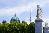 Germany, Berlin, Mitte, Museum Island. Berliner Dom, Berlin Cathedral, green copper domes with the Fernsehturm TV Tower beyond and statues on a bridge across the Spree Canal.