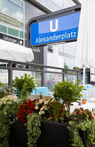 Germany, Berlin, Mitte, cafe tables with seating and planted growing flowers by an entrance to Alexanderplatz U-bahn underground railway station.