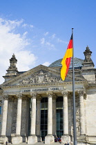 Germany, Berlin, Mitte, The Reichstag building in Tiergarten with the inscrption Dem Deucschen Volke, For the German People, on the facade above the columns at the entrance with a German flag on a fla...
