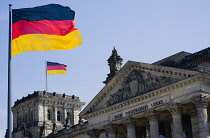 Germany, Berlin, Mitte, The Reichstag building in Tiergarten with the inscrption Dem Deucschen Volke, For the German People, on the facade above the columns at the entrance with German flags flying al...