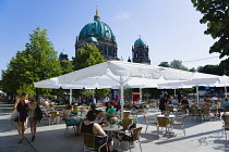 Germany, Berlin, Mitte, Museum Island. Berliner Dom, Berlin Cathedral, green copper domes beyond people sitting at cafe tables in the shade under umbrellas.
