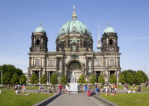 Germany, Berlin, Mitte, Museum Island. Berliner Dom, Berlin Cathedral. people cooling down in a fountain in Lustgarten in front of the church with copper green domes and the Fernsehturm TV Tower beyon...