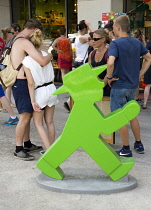 Germany, Berlin, Mitte, young people on the pavement beside a large green model of an Ampelmann or Ampel Man, the former East German pedestrian traffic light symbol created by Karl Peglau.