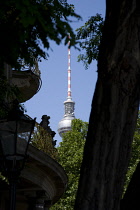 Germany, Berlin, Mitte, The Fernsehturm TV Tower near Alexanderplatz seen through trees against a blue sky.