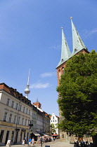 Germany, Berlin, Mitte, the old St Nicholas Quarter, the Nikolaiviertel, with the twin spires of Nikolaikirche and the distant Fernsehturm TV Tower with sightseeing tourists walking past tourist shops...