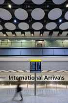England, London, Heathrow Airport, International Arrivals hall in Terminal 5 with person walking past an electronic arrivals board listing incoming due flights.