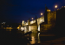 Czech Republic, Bohemia, Prague, The Charles Bridge across the River Vltava illuminated at night with the Little Quarter on the far side of the water and people on the bridge