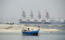 Angola, Luanda, Small moored fishing boat, with dredging and cargo ships in background.