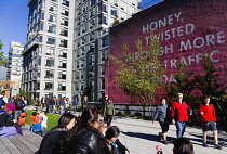 USA, New York, Manhattan, High Line linear park between buildings on a disused elevated railroad spur with people beside a wall painting by conceptual artist Ed Ruscha titled Honey I Twisted Through M...