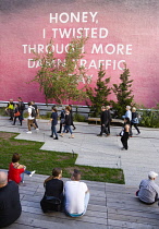 USA, New York, Manhattan, High Line linear park between buildings on a disused elevated railroad spur with people beside a wall painting by conceptual artist Ed Ruscha titled Honey I Twisted Through M...