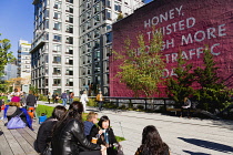 USA, New York, Manhattan, High Line linear park between buildings on a disused elevated railroad spur with people beside a wall painting by conceptual artist Ed Ruscha titled Honey I Twisted Through M...