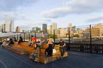 USA, New York, Manhattan, people on seating at sunset on the disused elevated West Side Line railroad making the High Line linear park beside the Hudson Rail Yards with trains at the north end in Midt...