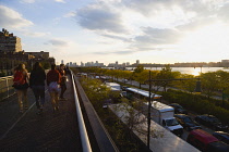 USA, New York, Manhattan, People walking on the northern end of the High Line elevated linear park beside Twelfth Avenue and the Hudson River at sunset in autumn.