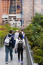 USA, New York, Manhattan, people walking towards the Wildflower Field on the High Line linear park on a disused elevated railroad spur called the West Side Line running between high rise buildings in...