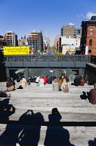 USA, New York, Manhattan, people seated on the the 10th Avenue Square viewing platform on the High Line a linear park on an elevated disused section of railroad looking at traffic on the road below.