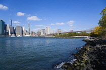 USA, New York, Lower manhattan skyscraper skyline, suspension bridge and East River seen from Brooklyn Bridge Park in autumn.