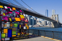 USA, New York, Brooklyn Bridge Park, colourful plexiglass house called Kolonihavehus by sculptor Tom Fruin below the bridge spanning the East River with Lower Manhattan beyond.
