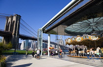 USA, New York, Brooklyn Bridge Park, children and adults at Jane's Carousel within a glass pavilion in the Empire Fulton Ferry section below the suspension bridge across the East River with the Lower...