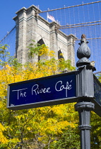 USA, New York, Brooklyn Bridge Park, signpost for The River cafe and detail of one of the suspension bridge towers against a blue sky in autumn colours.