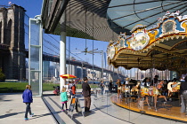 USA, New York, Brooklyn Bridge Park, children and adults at Jane's Carousel within a glass pavilion in the Empire Fulton Ferry section below the suspension bridge across the East River with the Lower...