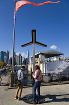 USA, New York, Brooklyn Bridge Park, People at an AT&T solar panel Street Charger for mobile phones on Fulton Ferry Landing with skyscraper skyline of Lower Manhattan beyond.