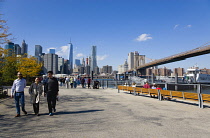 USA, New York, Brooklyn Bridge Park, People on Fulton Ferry Landing in autumn with the skyscraper skyline of Lower Manhattan beyond.
