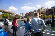 USA, New York, Brooklyn Bridge Park, passengers on the deck of the boat to the Wall Street Ferry Pier leaving the Fulton Ferry Landing below the suspension bridge.