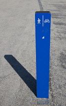 USA, New York, Brooklyn Bridge Park, blue signpost on path for cyclists and pedestrians casting a shadow.
