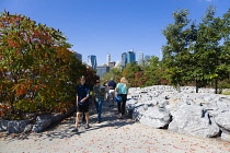 USA, New York, Brooklyn Bridge Park, people walking on a path in the landscape planted area between Pier 1 and Pier 2 with the Lower Manhattan skyscraper skyline beyond.