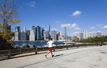 USA, New York, Brooklyn Bridge Park, jogger on a path in autumn between Pier 1 and Pier 2 with the Lower Manhattan skyscraper skyline and the East River beyond.