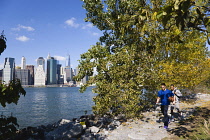 USA, New York, Brooklyn Bridge Park, two young men carrying a basketball on a path between Pier 1 and Pier 2 with the Lower Manhattan skyscraper skyline and the East River beyond.
