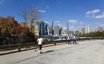 USA, New York, Brooklyn Bridge Park, jogger and walkers on a path in autumn between Pier 1 and Pier 2 with the Lower Manhattan skyscraper skyline and the East River beyond.