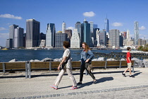 USA, New York, Brooklyn Bridge Park, walkers on a path between Pier 1 and Pier 2 with the Lower Manhattan skyscraper skyline and the East River beyond.