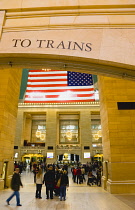 USA, New York, Manhattan, Grand Central Terminal main concourse busy with people and the Stars and Stripes flag hanging down above them.