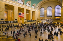 USA, New York, Manhattan, Grand Central Terminal main concourse busy with people and the Stars and Stripes flag hanging down above them.