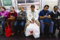 USA, New York, Queens, seated subway passengers on the E Train all using their mobile cell phones but not making telephone voice calls.
