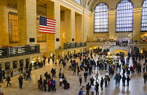 USA, New York, Manhattan, Grand Central Terminal main concourse busy with people and the Stars and Stripes flag hanging down above them.
