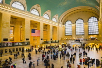 USA, New York, Manhattan, Grand Central Terminal main concourse busy with people and the Stars and Stripes flag hanging down above them.