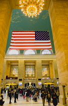 USA, New York, Manhattan, Grand Central Terminal main concourse busy with people and the Stars and Stripes flag hanging down above them.