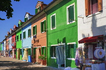 Italy, Veneto, Burano Island, Colourful row of house facades with outdoor display of lace for sale.