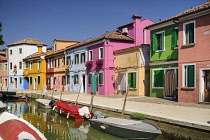 Italy, Veneto, Burano Island, Colourful row of house facades with boats on a small canal in the foreground.