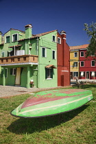 Italy, Veneto, Burano Island, Rows of houses painted in green and brown with boat in foreground which has the same colours.
