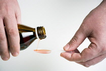 Health, Medical, Medicine, Hand holding a bottle of cough mixture and pouring it into a plastic spoon against a white background.