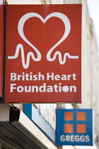 Business, Shops, Charity, British Heart Foundation sign on a high street shop with a Greggs pie shop sign beyond it. **Editorial Use Only**