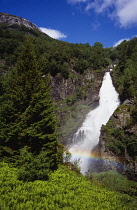 Norway, Sogn og Fjordane, Naeroydalen, Stalheimfossen waterfall cascading into steep  wooded valley with rainbow across lower level.