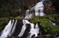 Norway, Rogaland, Svandalsfossen, Waterfall near town of Sauda.  Tiered levels of rocks with multiple streams of white water flowing down  surrounded by trees and vegetation.