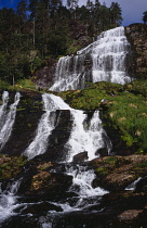 Norway, Rogaland, Svandalsfossen, Waterfall near town of Sauda.  Tiered levels of rocks with multiple streams of white water flowing down  surrounded by trees and vegetation.